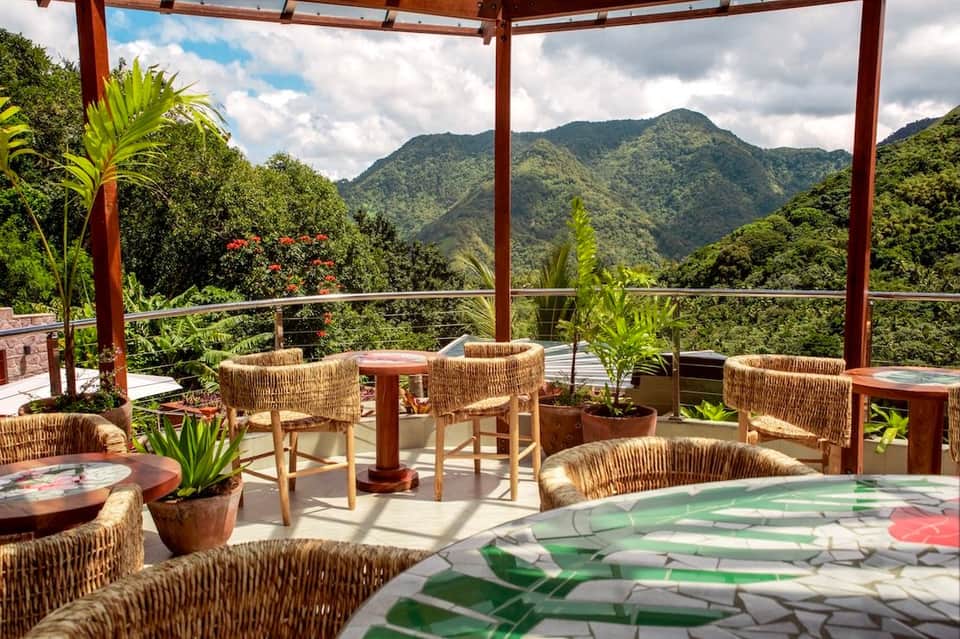 Tropical resort terrace with woven chairs, mountain views, and red pergola overlooking lush valleys