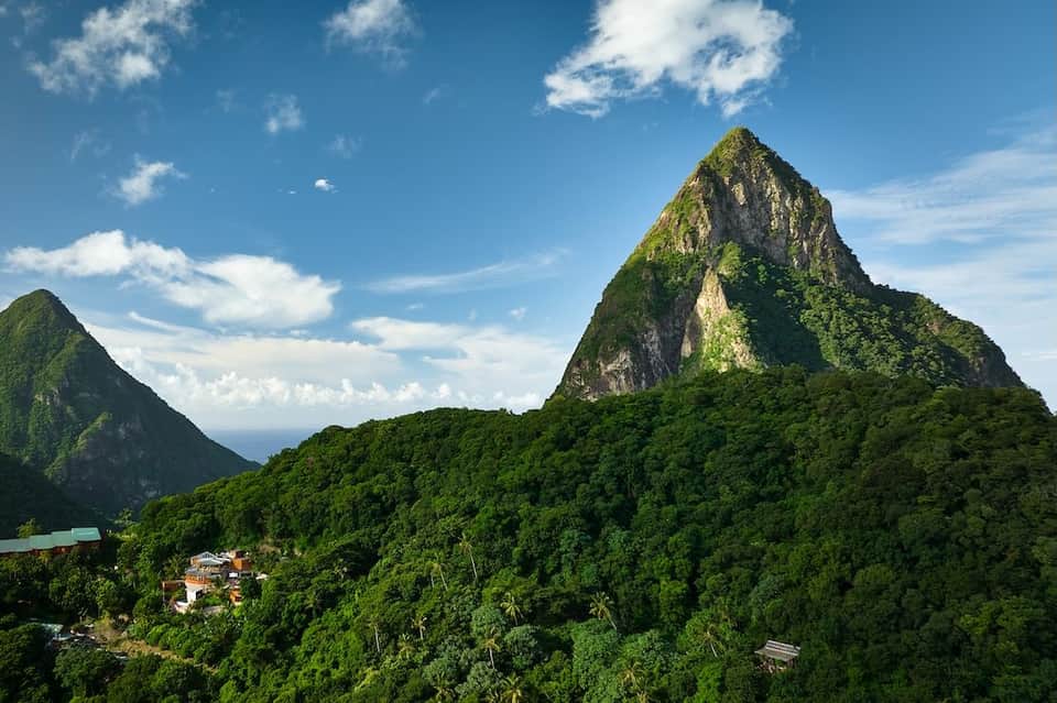 Dramatic peaked mountains covered in dense tropical forest under blue sky with white clouds