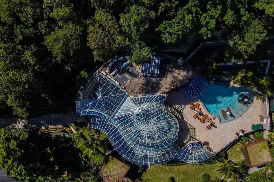 Overhead view of resort with geometric blue-roofed structures, pools, and surrounding forest canopy