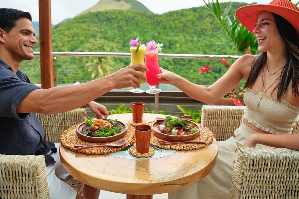 Couple toasting tropical cocktails on a terrace overlooking lush green mountains