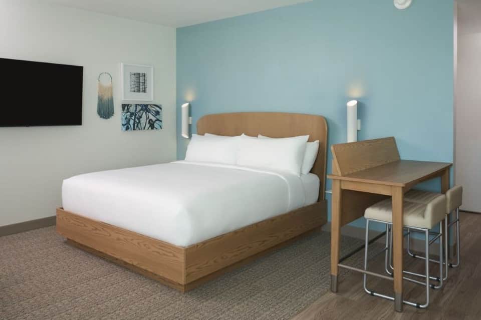 Contemporary hotel bedroom with light blue accent wall, wooden bed, and desk area