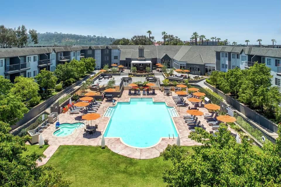 Aerial view of resort courtyard with turquoise swimming pool, lounge chairs, and surrounding residential buildings