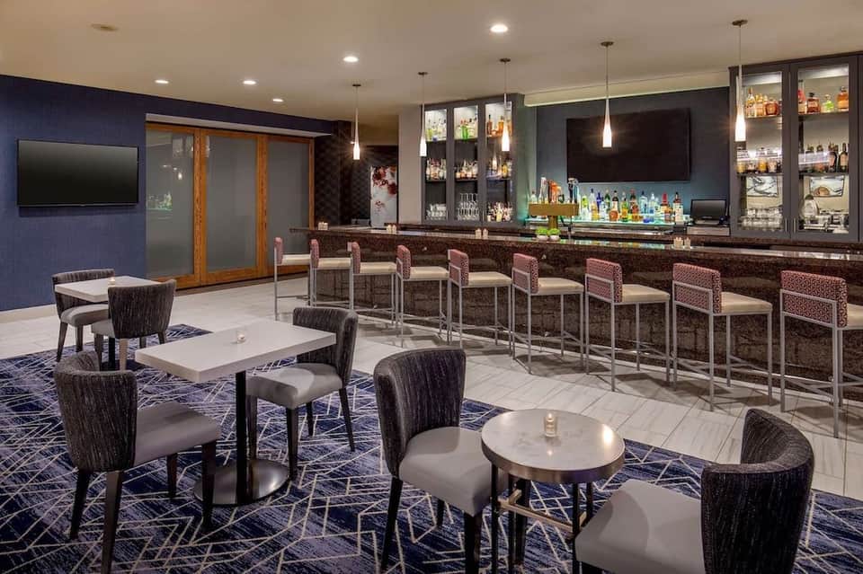 Modern hotel bar lounge with navy walls, upholstered seating, and bar counter with pendant lighting