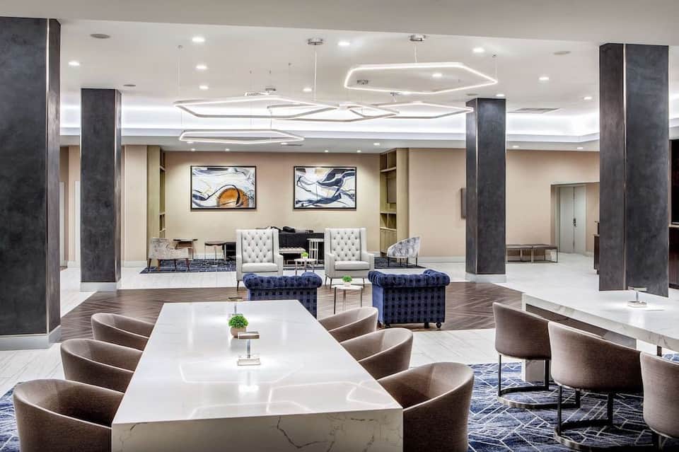 Modern hotel lobby with white marble table, contemporary seating, dark columns, and artistic ceiling lighting