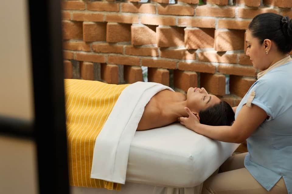 Spa therapist providing facial massage to client in treatment room with brick wall