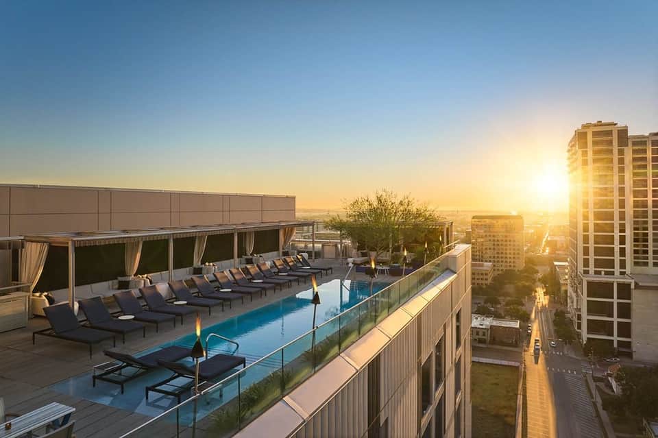 Rooftop pool with lounge chairs at sunset overlooking city and buildings