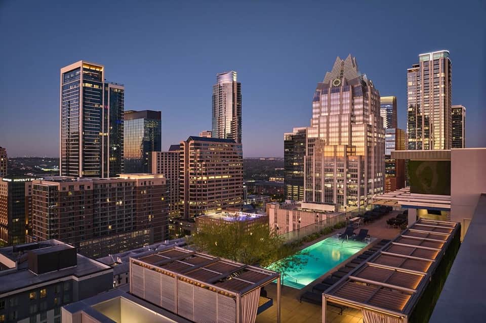 Downtown rooftop pool at dusk with illuminated cityscape and modern buildings