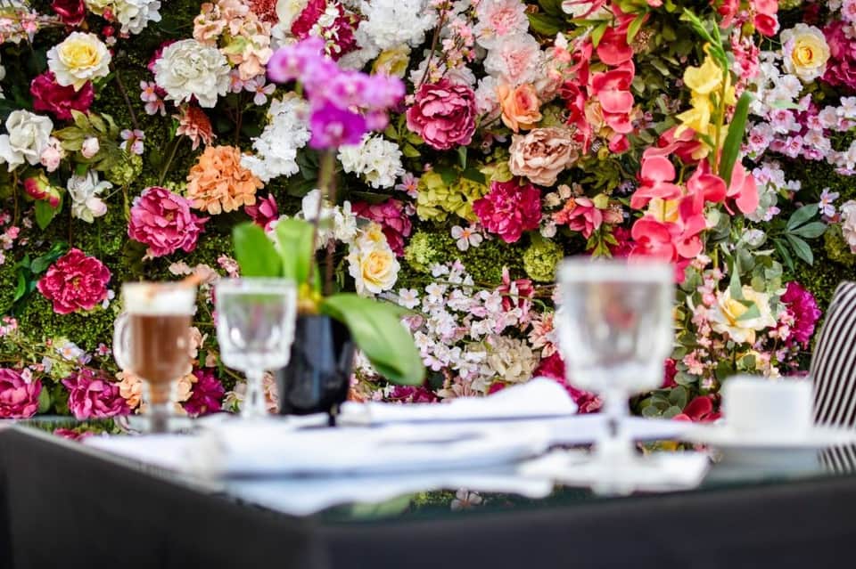 Colorful floral wall backdrop with dining table setting, wine glasses, and place settings in foreground