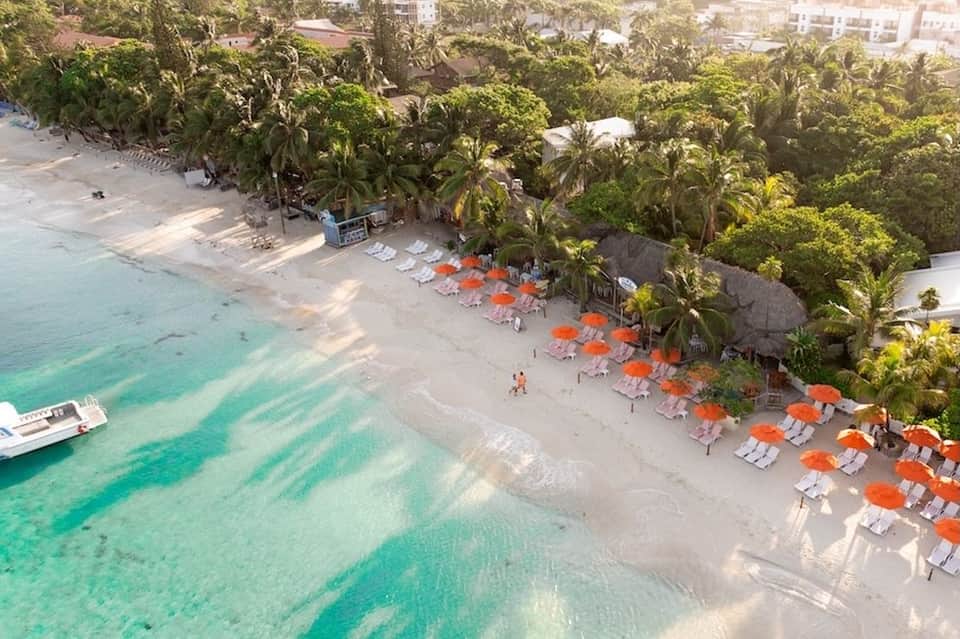 Aerial view of tropical beach resort with orange umbrellas, palm trees, and clear turquoise water