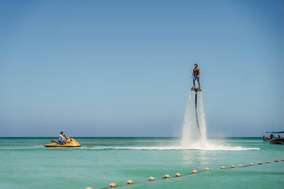 Man performing flyboarding over turquoise ocean water with jet ski support