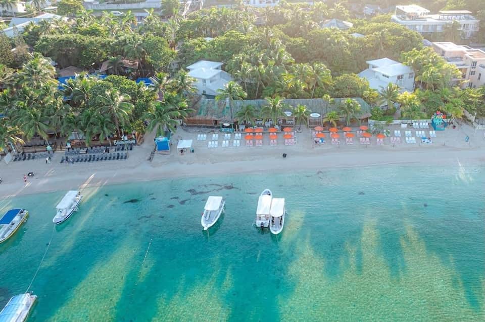 Aerial view of beach resort with boats, orange umbrellas, sand, and lush palm trees
