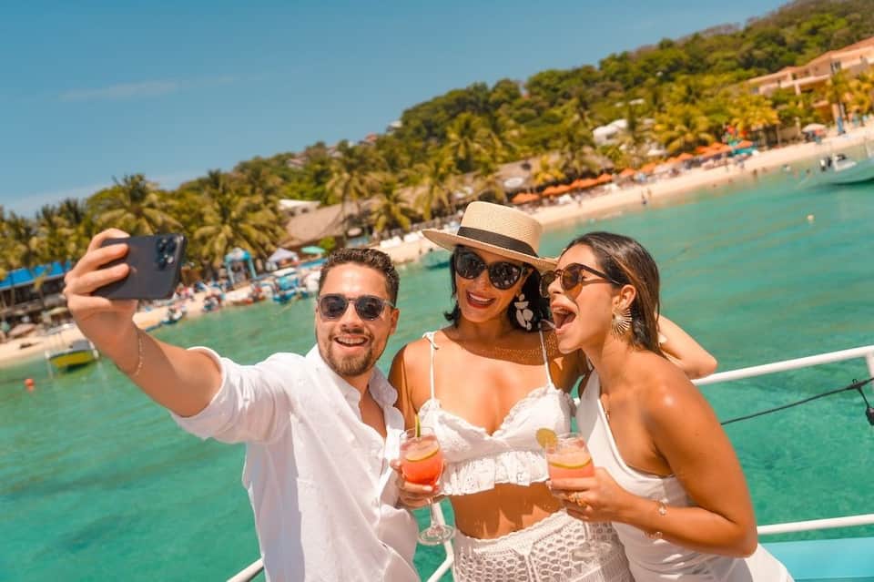Three guests taking a selfie with tropical beach and resort in background