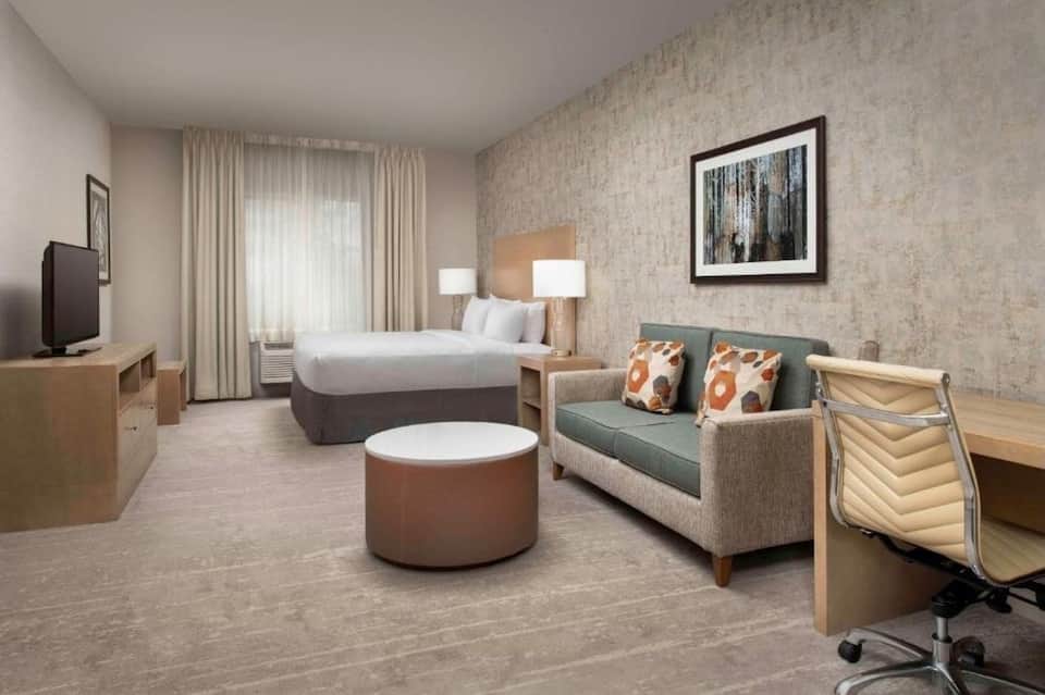 Spacious hotel suite with king bed, seating area, desk, and patio access