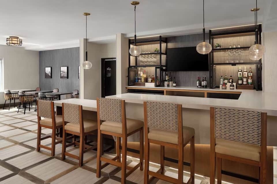 Hotel bar with wood accents, pendant lighting, and bar seating with patterned chairs