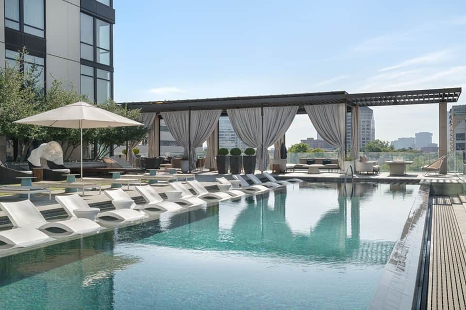 Luxury rooftop pool with modern loungers, draped pergola, and city skyline views