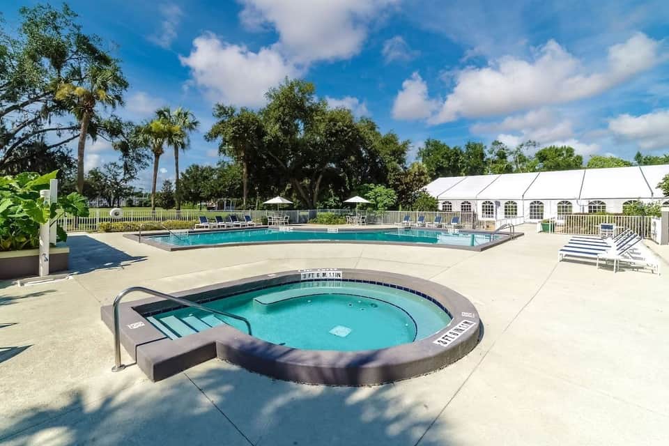 Resort pool and spa area with loungers, white tent structure, and palm trees