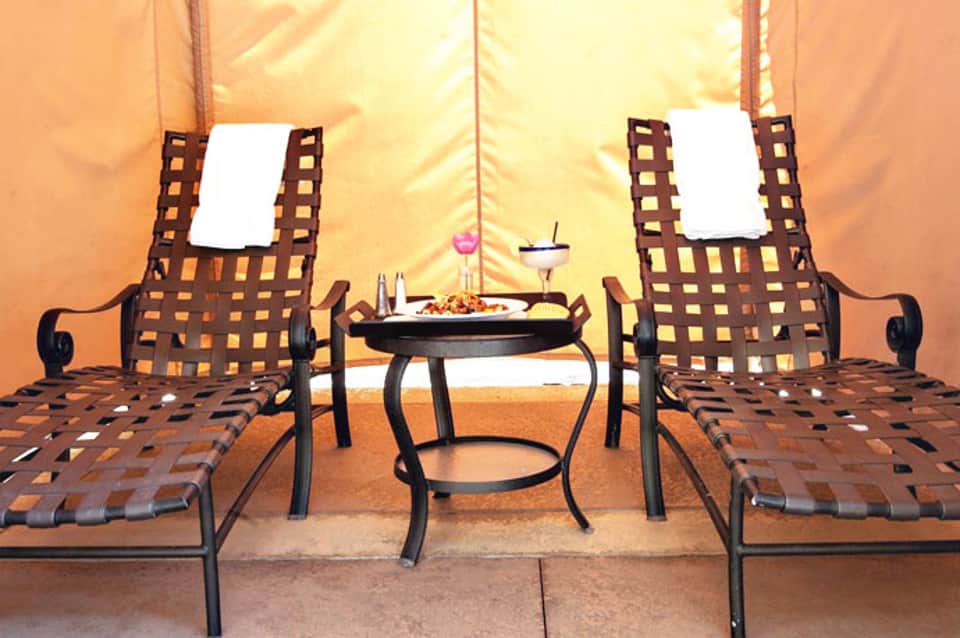 Luxury glamping tent interior with two striped loungers facing a small table with refreshments