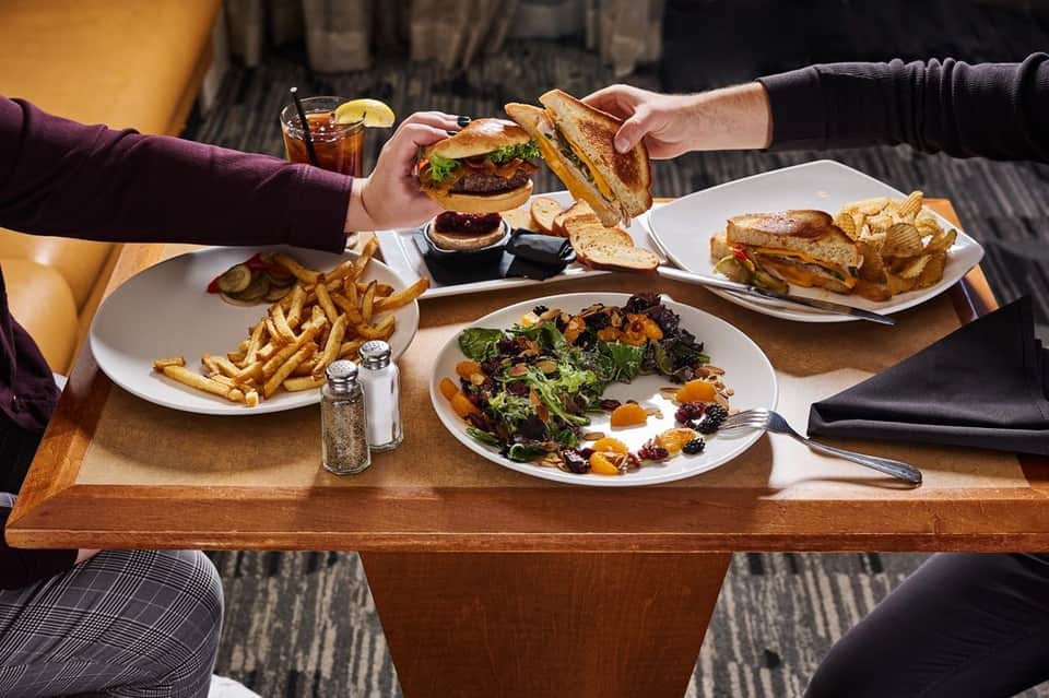 Two diners sharing burgers and fries at a casual restaurant table with cocktails