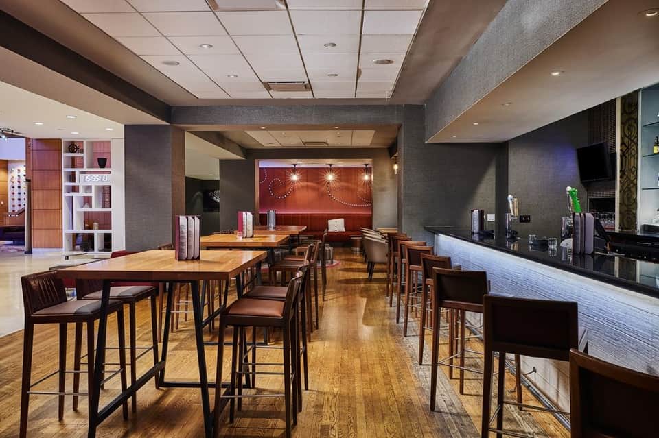Upscale hotel lounge with wooden tables, bar seating, and contemporary decor