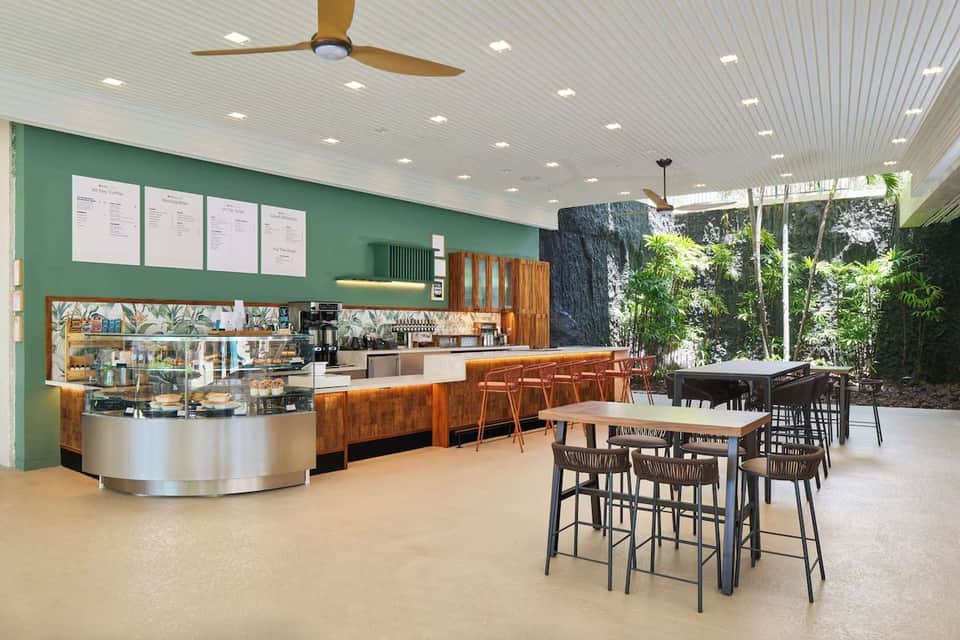 Modern beachside café with green walls, wooden counter, high seating, and tropical views