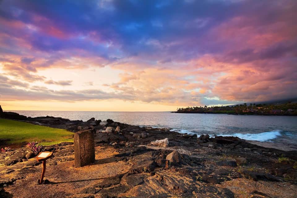 Dramatic sunset sky over rocky coastline, ocean, and palm tree-lined shore