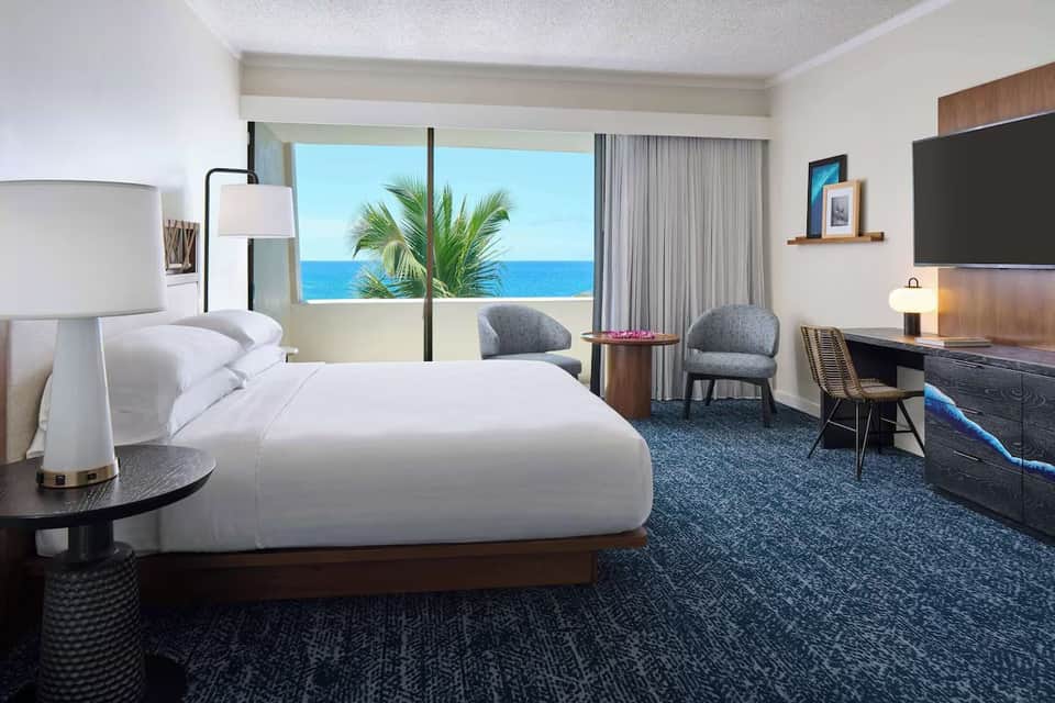 Ocean view hotel room with king bed, modern furnishings, and balcony overlooking water