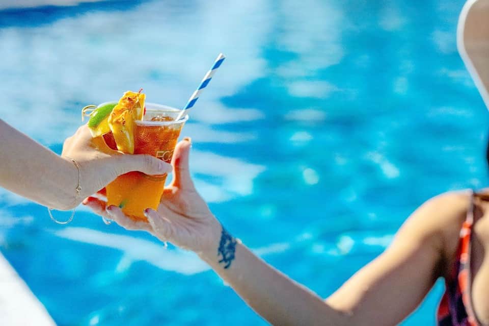 Tropical cocktail with citrus garnish held over bright blue swimming pool water