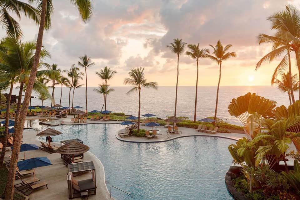 Resort pool at sunset with palm trees, loungers, and ocean horizon at dusk