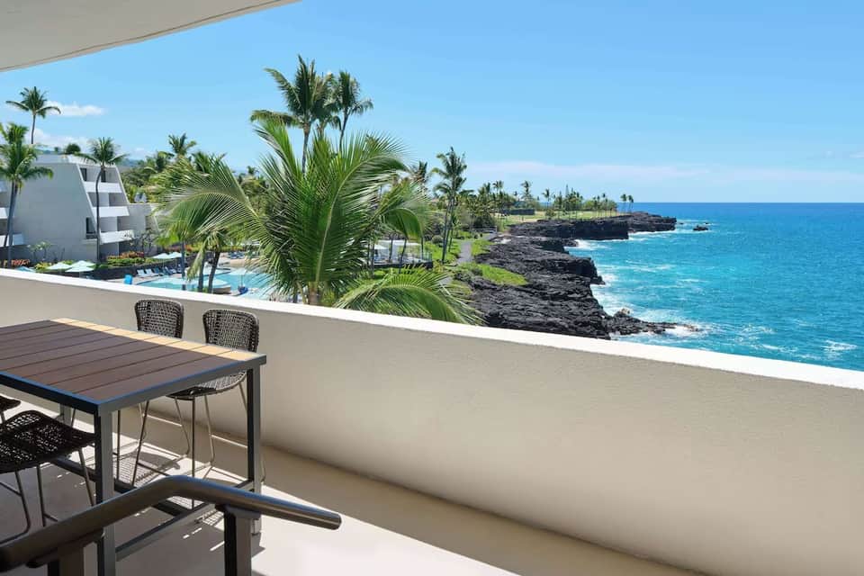 Modern balcony overlooking tropical landscape, black lava rocks, and bright blue ocean