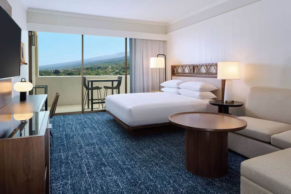 Upscale hotel room with ocean view balcony, white bed, and mountain landscape