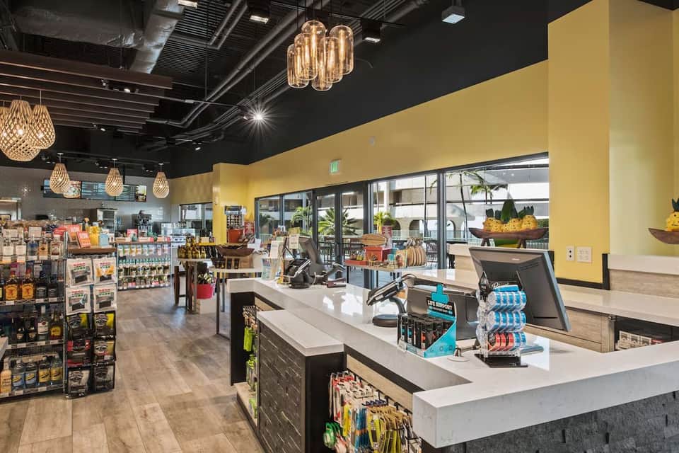 Modern resort lobby with yellow walls, pendant lighting, retail counter, and ocean view through large windows