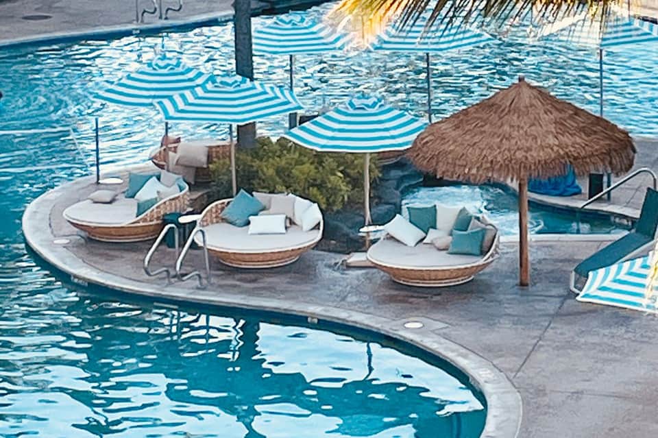 Aerial view of resort pool deck with striped umbrellas, boat-shaped loungers, and thatched cabana