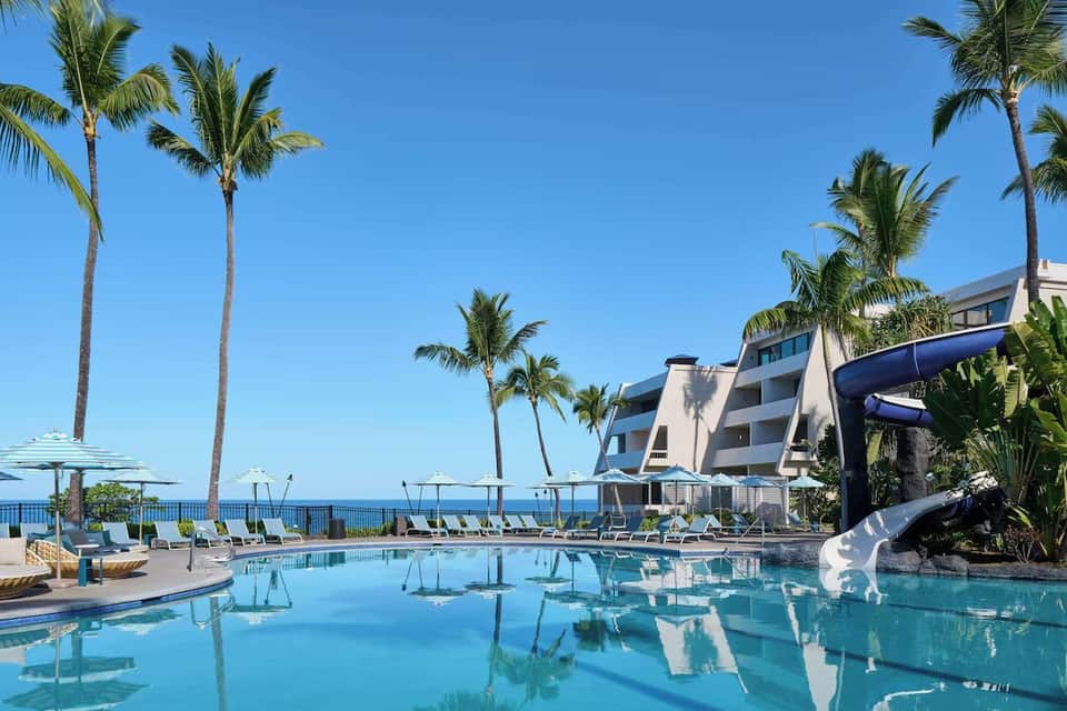 Oceanfront resort pool with turquoise water, palm trees, white loungers, and coastal hotel building