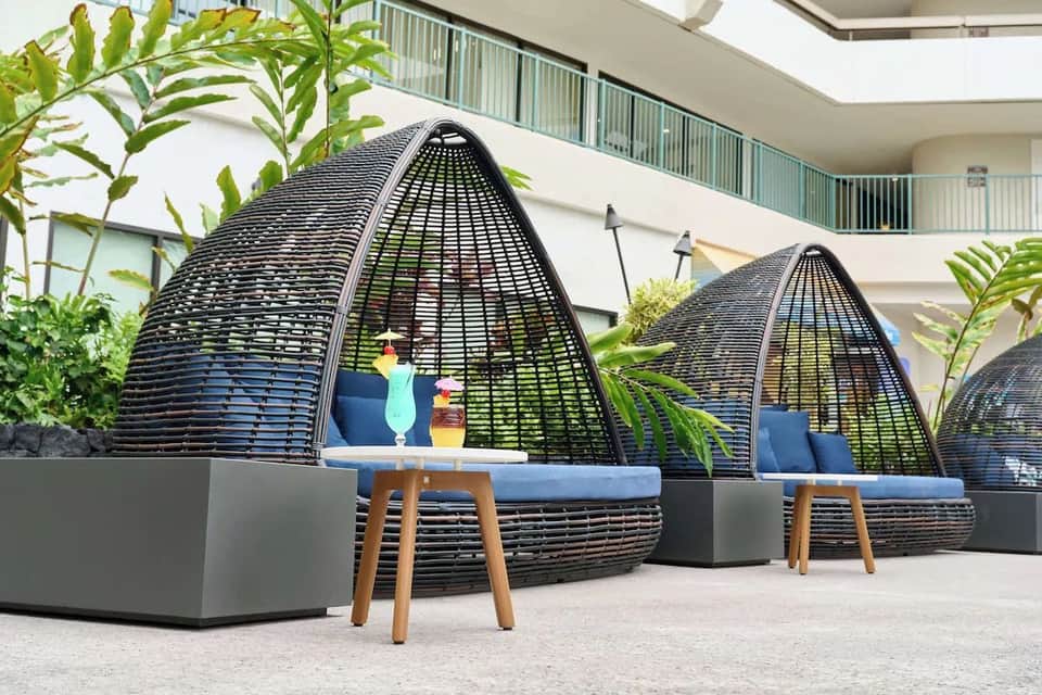Resort courtyard with black woven egg-shaped lounge chairs on white stone patio near modern building