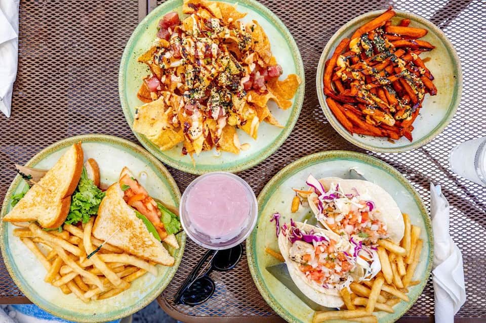 Overhead shot of five plates of tropical cuisine including fish, tacos, and appetizers with fries