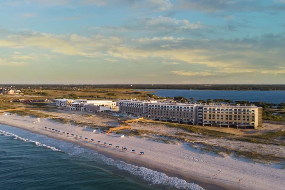 Beachfront resort aerial view showing buildings along sandy shore and bay landscape