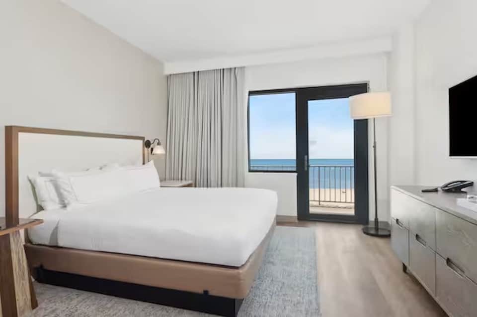 Modern hotel bedroom with ocean-view balcony, queen bed, and contemporary furnishings