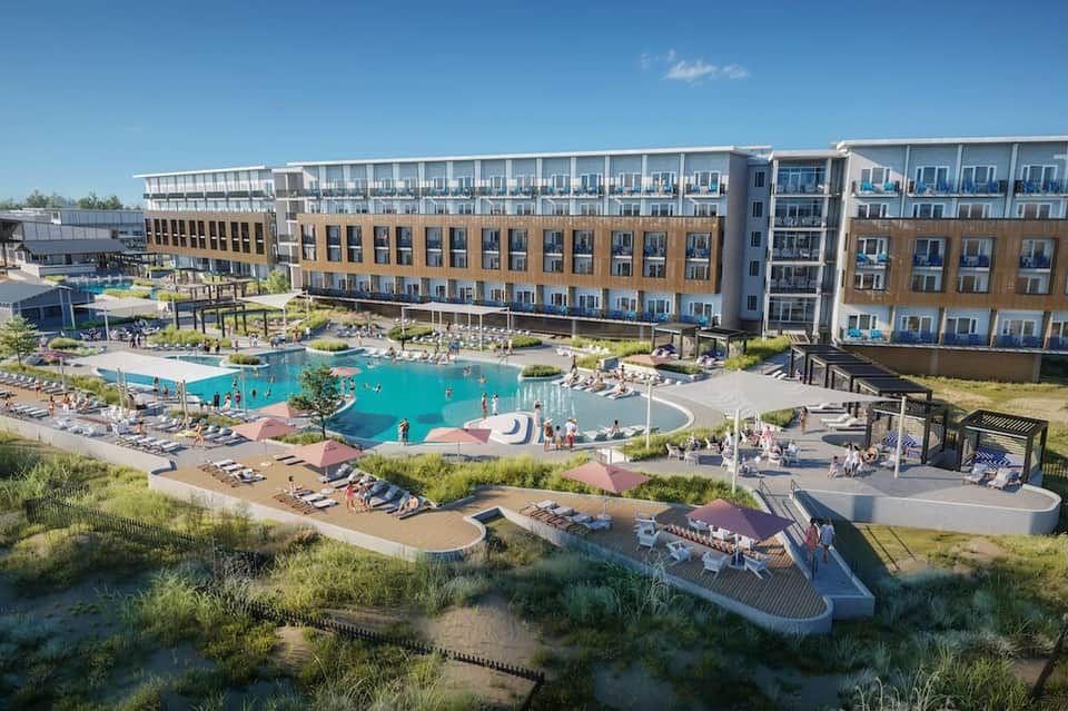 Aerial view of beachfront resort with turquoise pool, multi-story buildings, and sandy beach area