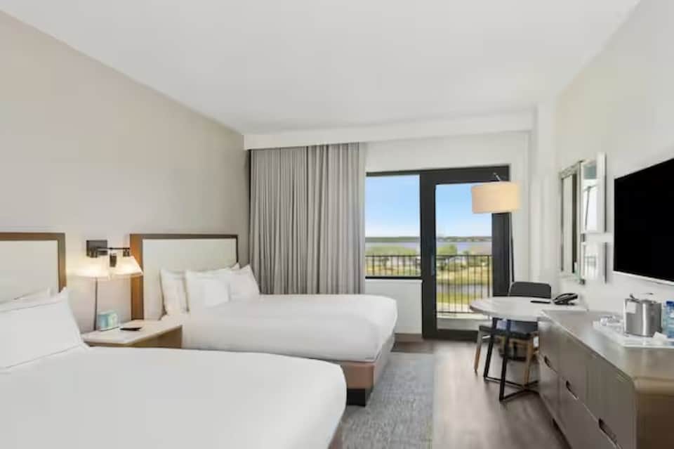 Double queen hotel room with bay view balcony, work desk, and modern decor