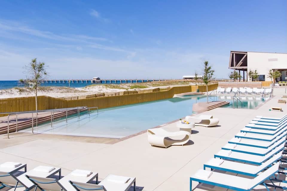Modern beachfront pool deck with lounge chairs and ocean view, wooden fence barrier visible