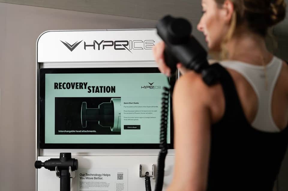 Woman using Hyperice recovery station with massage device in fitness facility