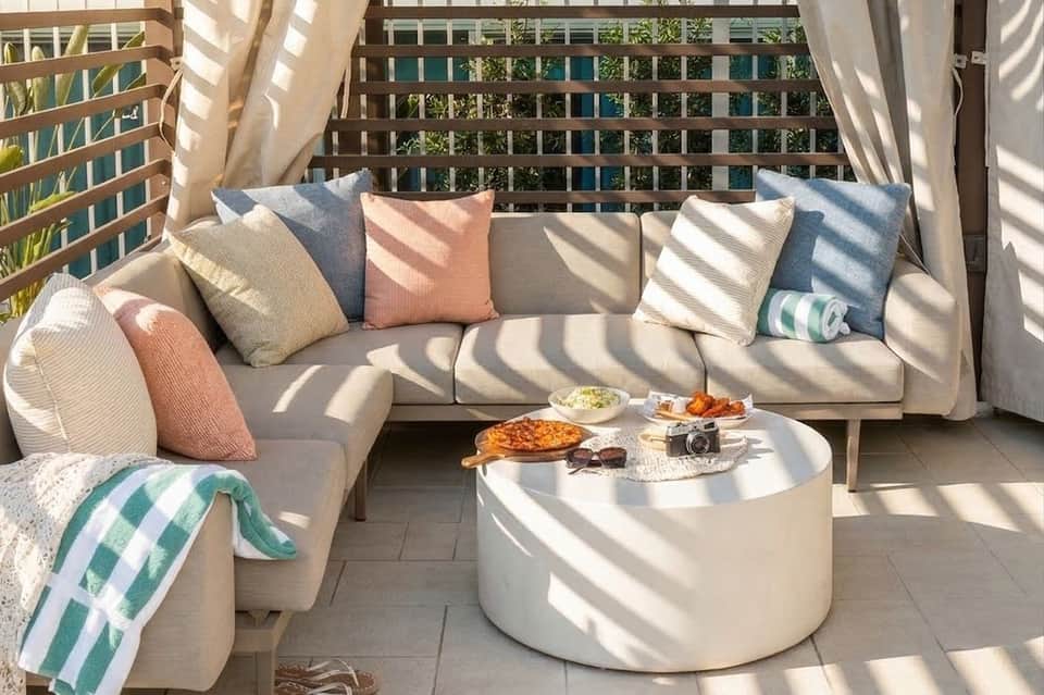 Coastal balcony seating area with cream sectional sofa, colorful pillows, white round coffee table, and striped beach towel