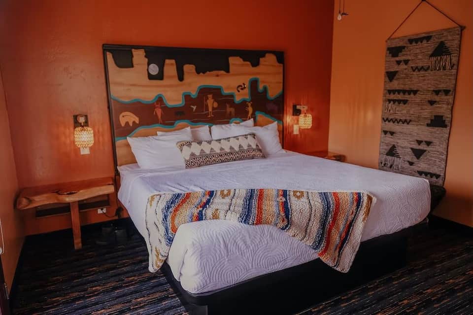Southwestern-themed hotel room with orange walls, native artwork, and patterned blankets