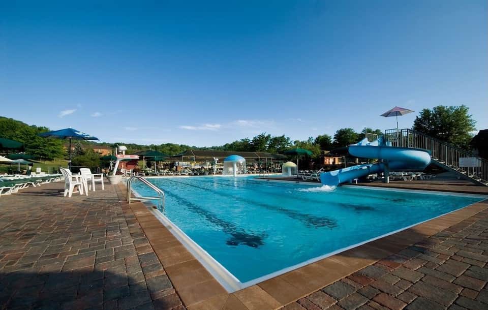 Outdoor swimming pool with blue water slide, white lounge chairs, and umbrella with scenic grounds