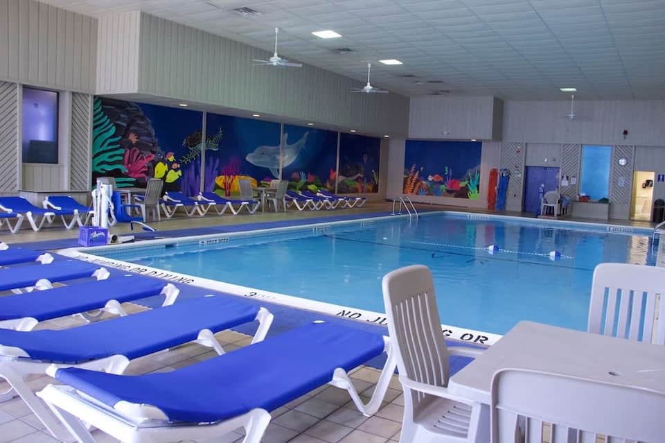 Indoor competitive swimming pool with lane dividers, blue loungers, and colorful underwater mural backdrop