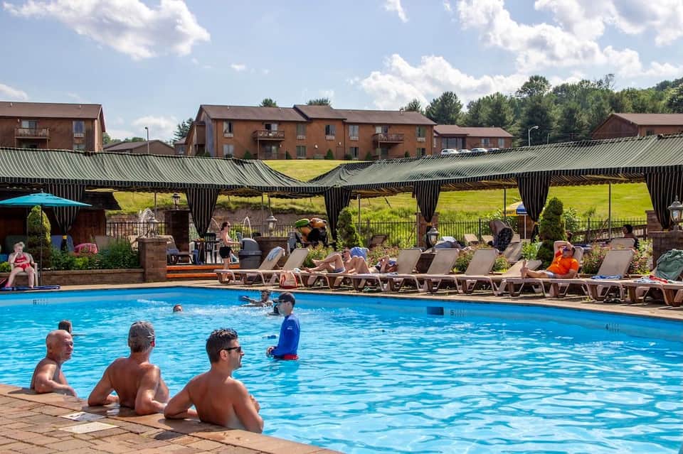 Large resort pool with covered patio, loungers, and residential buildings in background