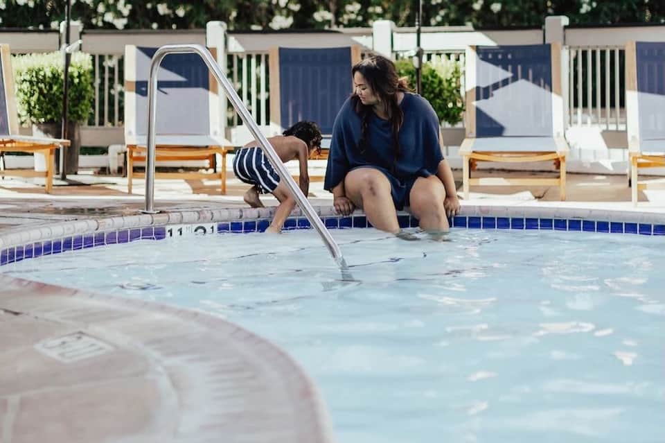 Woman and child at pool edge with slide, lounge chairs and cabanas in background