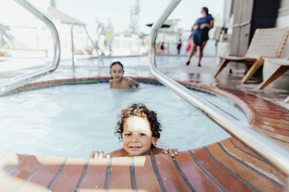 Young child smiling while holding pool rail in hot tub with another child visible