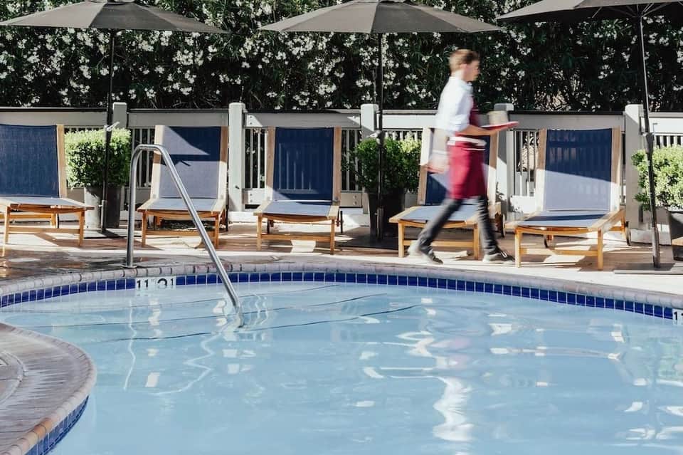 Resort pool with metal railings, lounge chairs, umbrellas, and person jogging past