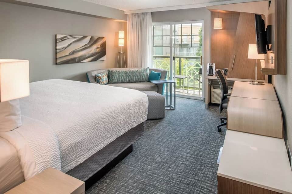 Spacious hotel room with king bed, comfortable seating area, balcony doors, and modern décor